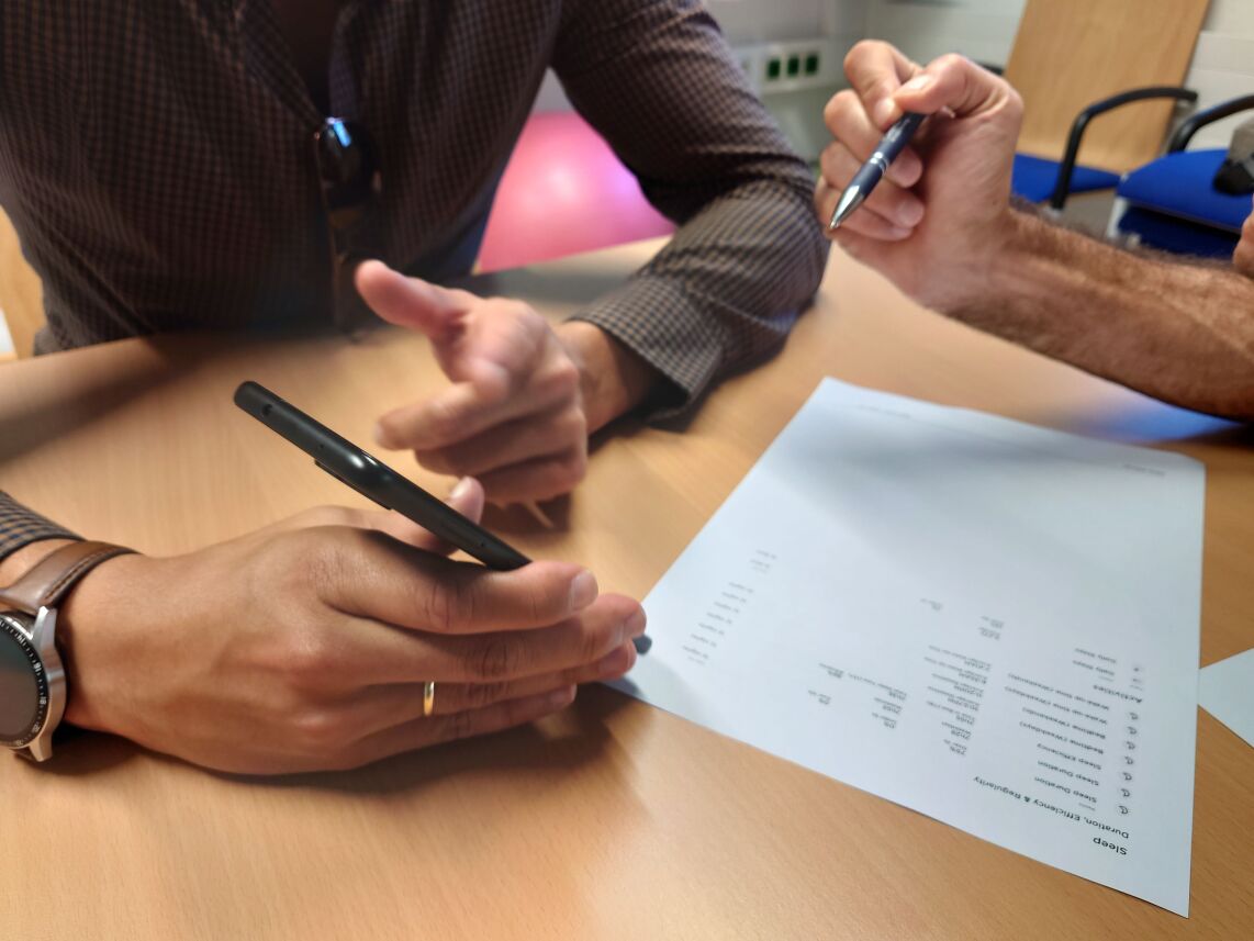 Photograph of a consultation showing hands with a pen while discussing results on a printed form.
