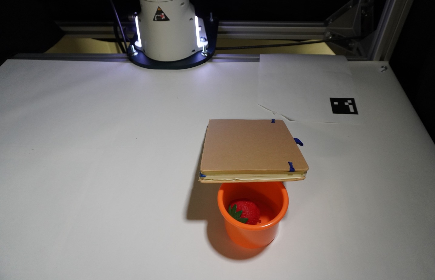 The robot successfully completes a multi-step task involving object manipulation and visual query answering, first pushing objects apart to isolate an eraser, then lifting and repositioning it based on a query about the text on the eraser's surface, and finally navigating around an occluding object to view a cup.